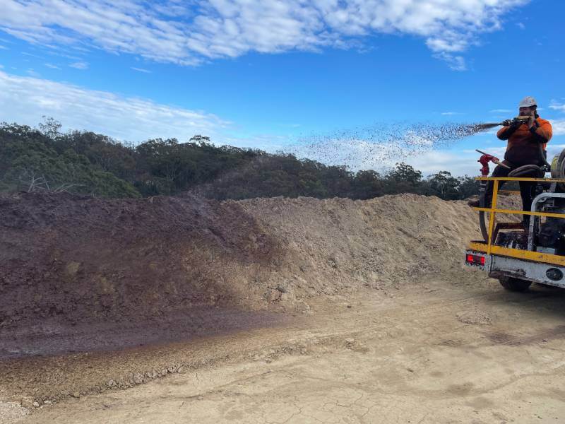 Person spraying a solution of water, seed, fertiliser, and a bonding agent onto a layer of soil.